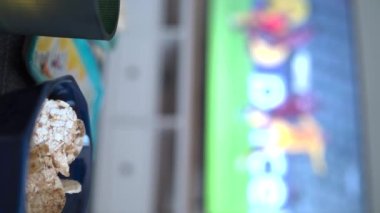 vertical video of man eating junk in font of blured tv watching soccer. High quality 4k footage