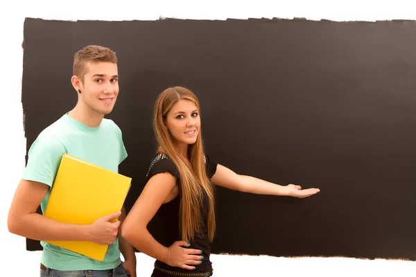 Woman pointing to the blackboard and man with book standing — Stock Photo, Image