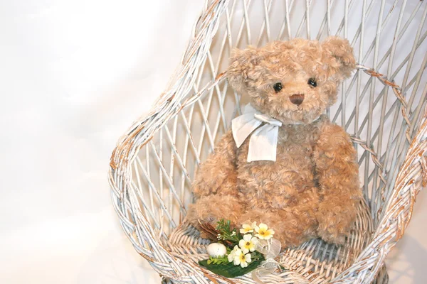 Lindo oso de peluche en una silla de mimbre blanco vintage con flores —  Fotos de Stock