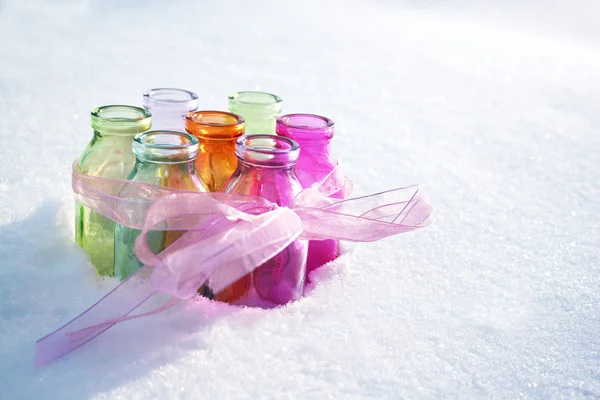 Garrafas de vidro coloridas com uma fita rosa na neve em um dia nevado de inverno — Fotografia de Stock