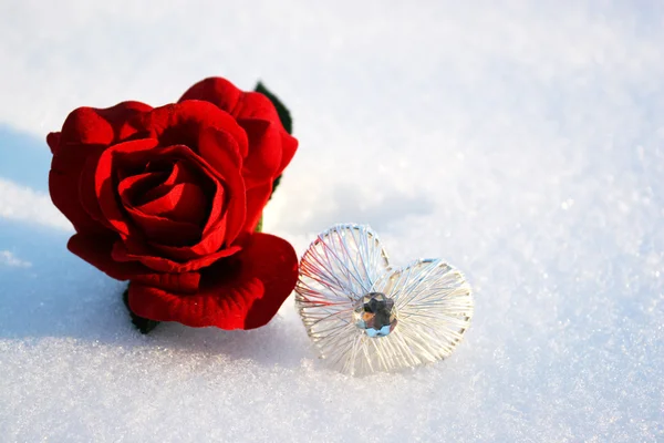 Vacker röd ros i snö med kristall hjärta i en vinterdag Stockbild