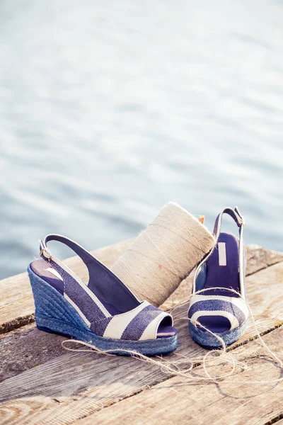 Denim blue sandals lie on wooden clutch at the lake — Stock Photo, Image