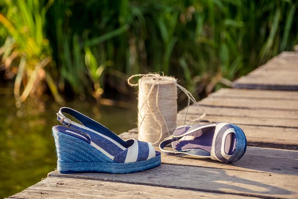 Sandálias de denim azul jazem na embreagem de madeira no lago — Fotografia de Stock