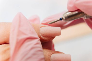 Manikür işlemi. Usta, otomatik bir makine kullanarak tırnağı parlatıyor. Matkap cilası çıkarıcı.