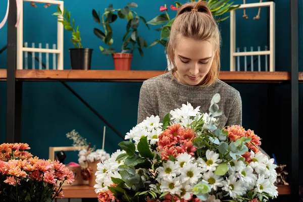 Florist makes a bouquet of multi-colored chrysanthemums. A young adult girl works with enthusiasm.