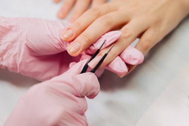 Manikür işlemi. Usta cımbız kullanarak özel bir jelden yapay bir çivi yapıyor..