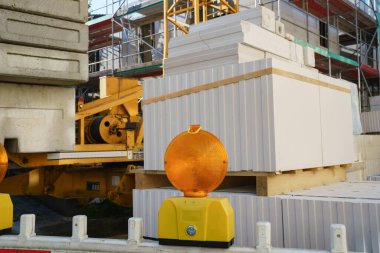 A warning orange light at a construction site. Stacked building materials and part of a building under construction.