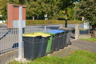 Metal bir çitin yanında bir grup plastik çöp ve geri dönüşüm kutusu. Şehir sokak manzarası.