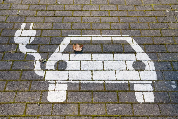 The electric car on the charging station pictogram icon is painted with white paint on the road tile.
