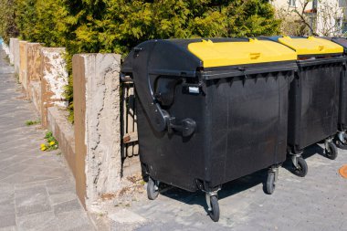 Sarı kapaklı iki çöp bidonu beton duvar boyunca üst üste yığılmış..