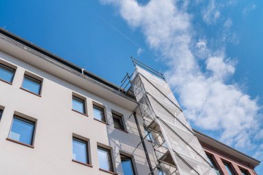 İskeleli beyaz bir binanın parçası. Mavi gökyüzü ve ışık bulutları.