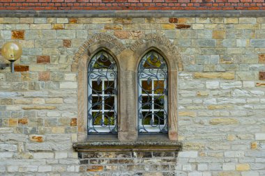 İki kemerli pencereli eski bir binanın taş duvarı. Pencereler dekore edilmiş metal şebeke ile kapatılmış. Duvardaki fener.