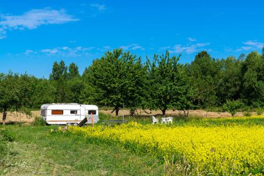 Beyaz karavanın karavanı yeşil bahçede. Plastik mobilya ve çocuk oyuncakları.