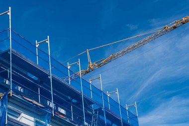 Binanın bir kısmı ve iskele ve ağ örgüleriyle çevrili sarı vinç yelkeni. Mavi gökyüzünün altında.