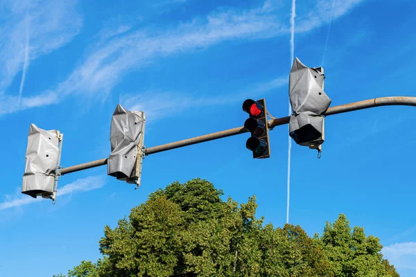 Street traffic lights on a horizontal bar under the blue sky. Three of them are non-working, wrapped with foil.