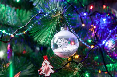 Noel süsü, beyaz cam top yeşil bir Noel ağacı dalı. Ağaçta Noel çelengi. Altın süslemeli sığ saha topu derinliği.