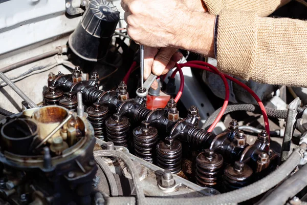 The mechanic uses a screwdriver and box wrench doing valve adjustment to repair gas distribution mechanism at old engine. Disassembled carburetor motor. DIY repair cylinder head with rocker shaft — Stock Photo, Image