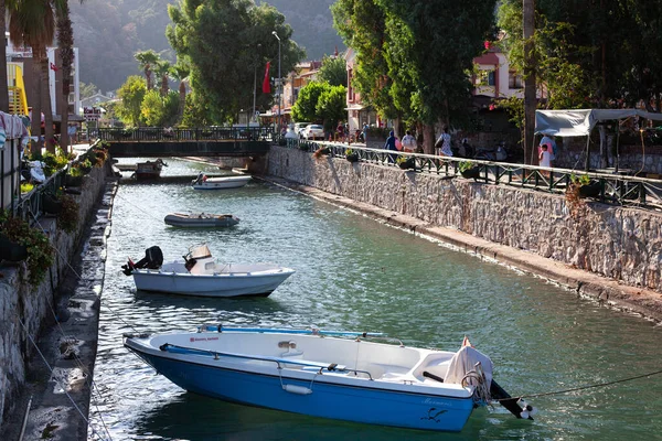 Barcos a motor amarrados en el canal de agua. Pequeño barco pesquero atado en el río en un pequeño pueblo turístico. La gente camina por el terraplén. — Foto de Stock