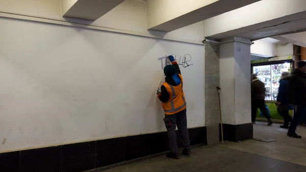Ta bort graffiti och måla från vandaler. en anställd i staden, klädd i en orange uniform, rengör väggen från graffiti och skriva, med ett flytande lösningsmedel. Stockfoto