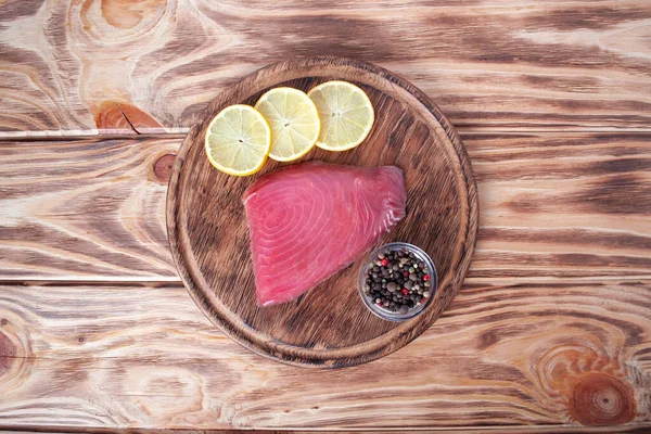 Fresh tuna fillet on wooden board. Fish steak on a cutting board with lemon slices and allspice. Red fish textured steak isolated — Stock Photo, Image