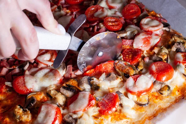 Mano con cuchillo cortador de pizza cortando pizza en la mesa de la cocina. De cerca.. — Foto de Stock