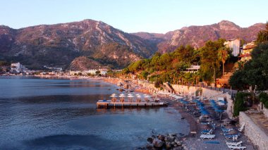 Türkiye 'nin Turunc kentindeki bir plajın hava görüntüsü. Güneşin doğuşu köyde İHA tarafından fotoğraflandı. Şemsiyeler ve güneş yatağı kumsalda.