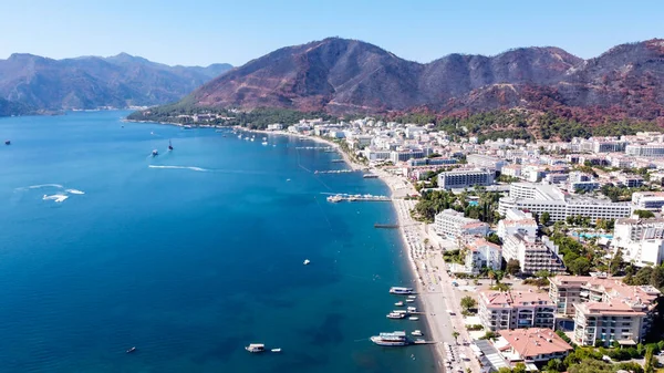 Türkiye 'de kalabalık plajlı, güneşli bir Marmaris şehrinin havadan görünüşü. Mavi deniz yüzeyinde tekne izleri var. Beyaz kumlu kumsal manzarası