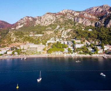 Turunc adlı küçük bir turistik köyde dağlarla ve kayalarla çevrili bir sahil. Sakin sulara demirlenmiş teknelerle dolu bir deniz manzarası. Drone görünümü.