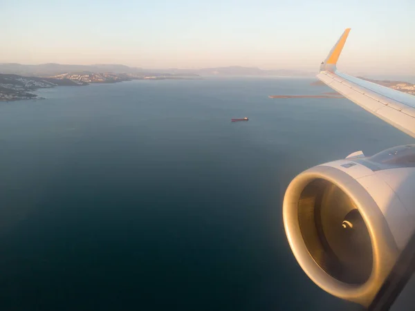 Airplane wing with engine out of window. Flight over sea coastline on sunrise. Airplane porthole view. Blurred image. Defocused — Fotografia de Stock