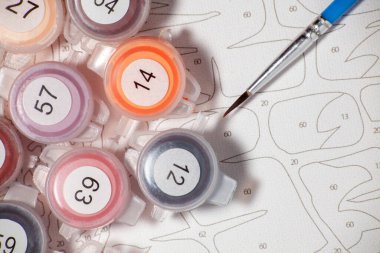 Kavanozlarda akrilik boyalar ve boya fırçası tuvali, arka planda işaretler. Sayılarla, hobilerle ve el sanatlarıyla resim yapmak. Ev hobisindeki numaradan boyama. Kapatın. Kavanoz kapağına odaklan