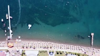 Kalabalık bir plaj manzarası, şemsiyeli, denizde yüzen insanlar, güneşli bir gün. Beyaz kumlu kumsal manzarası.