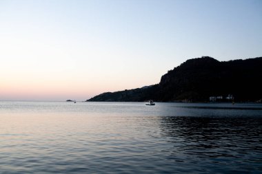 Deniz suyunda, dağ kayalarının üzerinde gün doğumu. Sakin denizde gün doğumu deniz manzarası. Dalgalanan suda kayalar ve altın yansımalar.