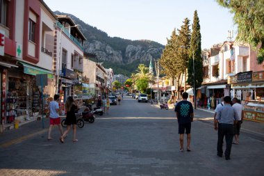 Tourists walk past a cafeteria and souvenir store in small resort town. Street food and souvenir shops on main street. Turunc, Turkey - September 7, 2022.