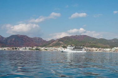 Big white pleasure ship cruises near Marmaris city in Turkey. Big white boat yacht against of the resort city. Ships in sea. Sea traveling. View from boat. Marmaris, Turkey - September 8, 2022.