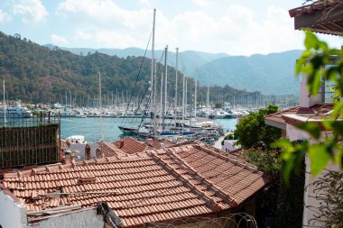Many yachts and boats in the harbor. Ships on pier in port. View over red tile shingles roofs in city. Marmaris, Turkey - 08.09.2021
