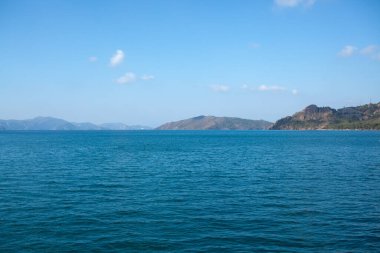 Yaz mevsimi deniz manzarası güzel dalgalar, güneşli bir günde mavi deniz suyu. Ufukta sisli dağlar olan deniz koyunda. Dağlarda sis..