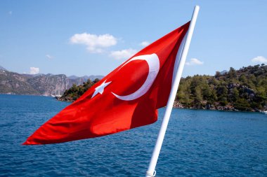Denize karşı mavi gökyüzünde dalgalanan Türk bayrağı, Türkiye. Bayrak direğinde hindi bayrağı.