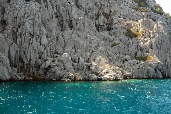 Turkuaz suyu olan Ege kayalık kıyıları. Lav taşları ve kayalar. Deniz manzaralı. Mavi sulardaki kaya yansıması