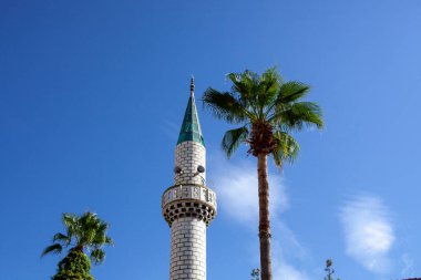 Beyaz cami minaresi. Türkiye 'nin arka planında bulutlar olan cami minaresi. Gökyüzüne karşı Müslüman camiinin uzun beyaz kulesi. Minarede hoparlörden Kur 'an okumak