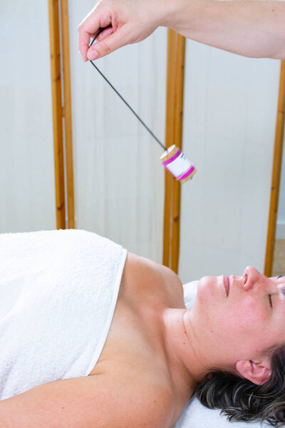 Женщина-массажистка размахивает еврейским маятником на груди другой женщины. Альтернативная или энергетическая терапия