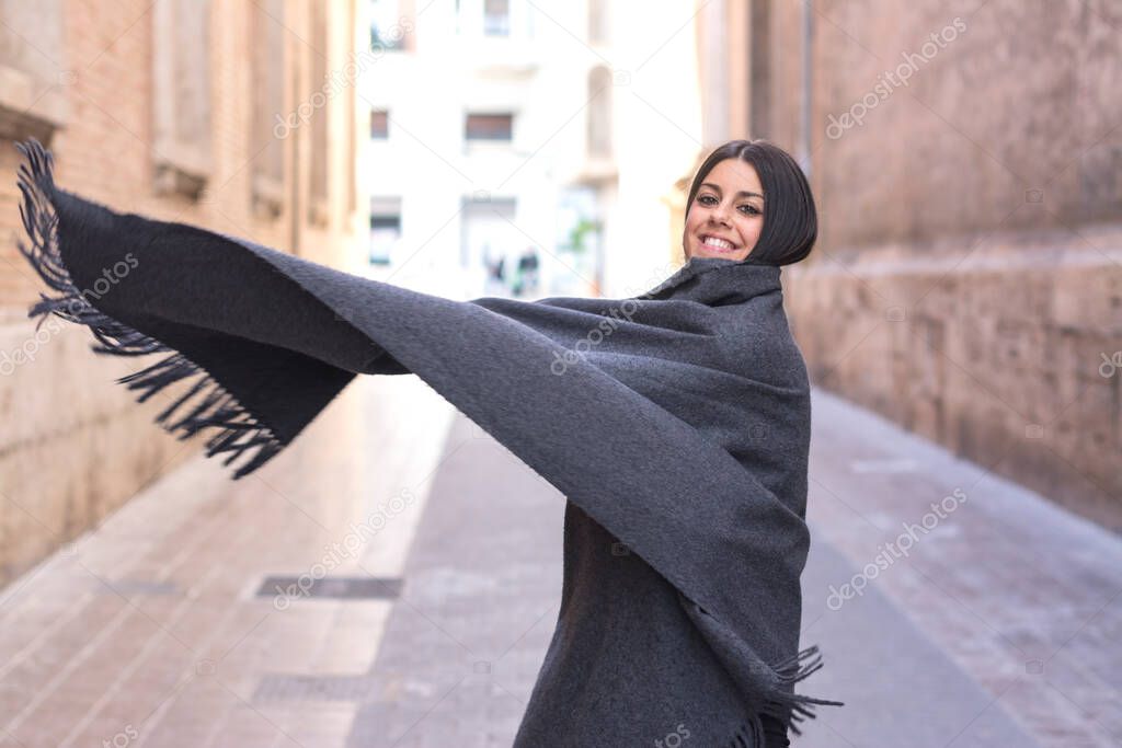 Woman covering herself with a cape, throwing it over her shoulder, in the street, in winter