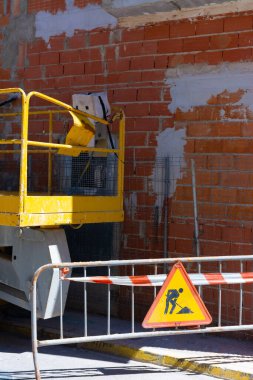 Küçük hidrolik inşaat platformu ve inşaat halindeki bir evin tuğladan duvarının yanında çalışan adamların işareti.