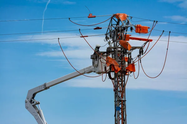 One unrecognizable worker in a hydraulic lift basket doing maintenance work on a power line