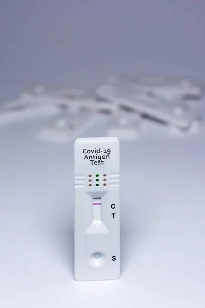 A covid-19 antigen test, with a negative result, with a stack of unfocused tests in the background, on a white background