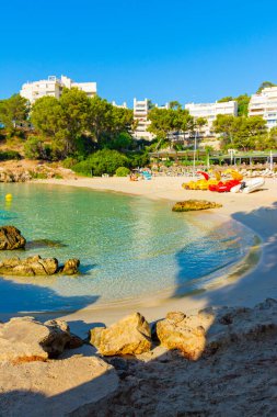 Calvia, Mallorca, İspanya. 18 Temmuz 2022 - Ses Illetes plajında kayalarla dolu bir köşede, sabahın erken saatlerinde, dinlenme tekneleriyle