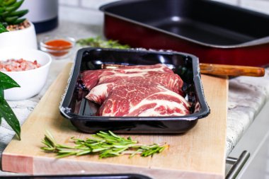 Tahta kesim tahtasındaki pakette pişirmeye hazır çiğ mermer biftek dilimleri var. Akşam yemeği için taze et hazırlıyorum..