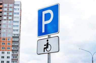 Gökyüzüne ve şehir binalarına karşı engelli insanlar için tekerlekli sandalyeli mavi-beyaz park levhası..