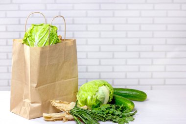 Çevrimiçi alışveriş merkezinden alınmış yeşil sebzelerle dolu el işi kağıt torbası arka planda fotokopi alanı ile birlikte mutfağa teslim ediliyor..