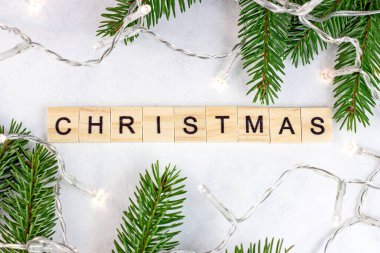 Yeşil köknar ağacı dalları ve ışıkları olan ahşap Noel yazılarının en üst görüntüsü tebrik kartları için beyaz arka planda Noel mevsimi dekorasyonu olarak. Geleneksel kış tatili tasarımı.