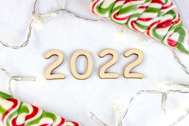 Ahşap numaraların üst görüntüsü 2022 yılbaşı ışıkları ve hafif arka planda tatlı şekerler. Yeni yıl başlıyor. Tebrikler ve planlama konsepti..